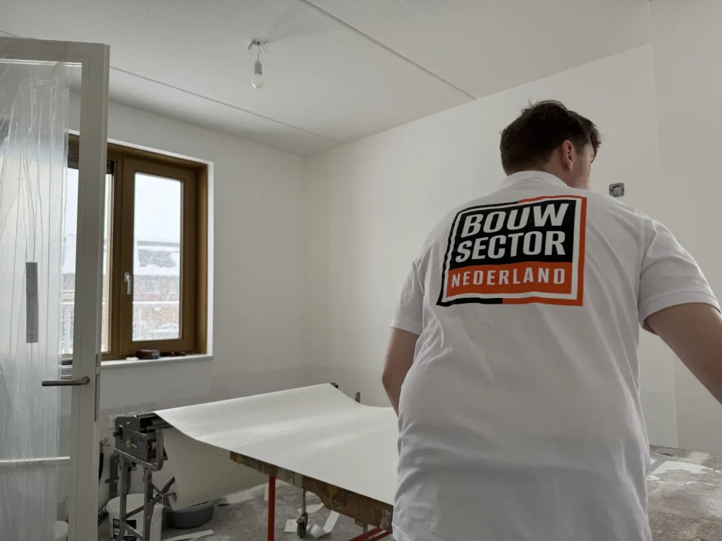 Behanger van Bouwsector Nederland rolt een baan vlies uit over de plaktafel in een lichte nieuwbouwkamer
