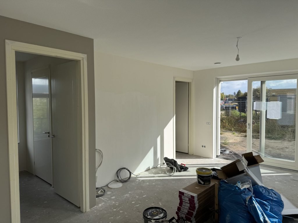 Nieuwbouwwoonkamer tijdens de afwerking, met tuindeuren en materiaal op de dekvloer
