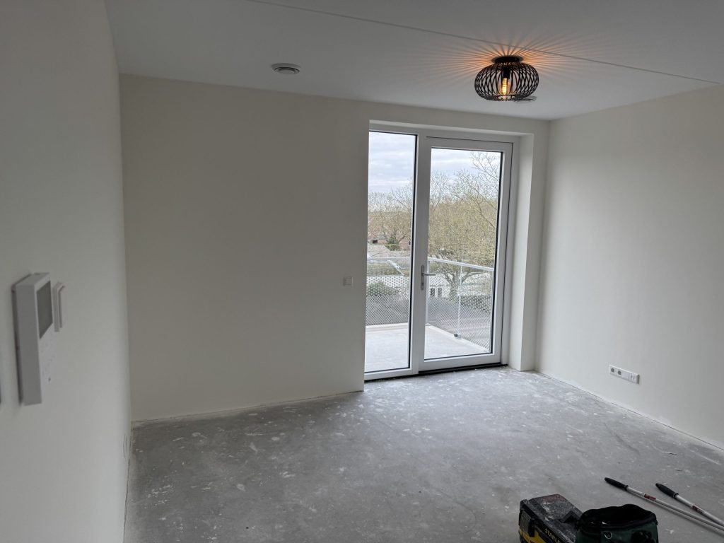 Lege nieuwbouwkamer met strak afgewerkte lichte wanden en openslaande deuren naar het balkon, kort na de oplevering